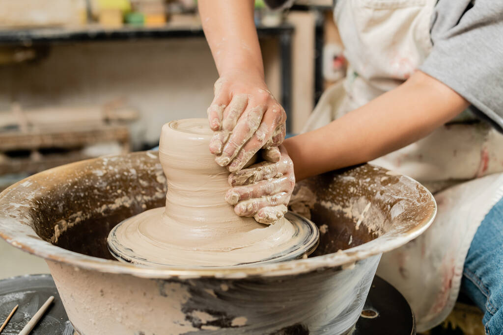 Oříznutý pohled rozmazané ženské keramiky v zástěře lití mokré hlíny a práce na spřádání keramiky kola v umění keramické studio, zkušený keramiky koncepce tvorby - Fotografie, Obrázek