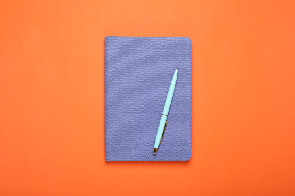 Caderno azul fechado e caneta no fundo laranja, vista superior - Foto, Imagem