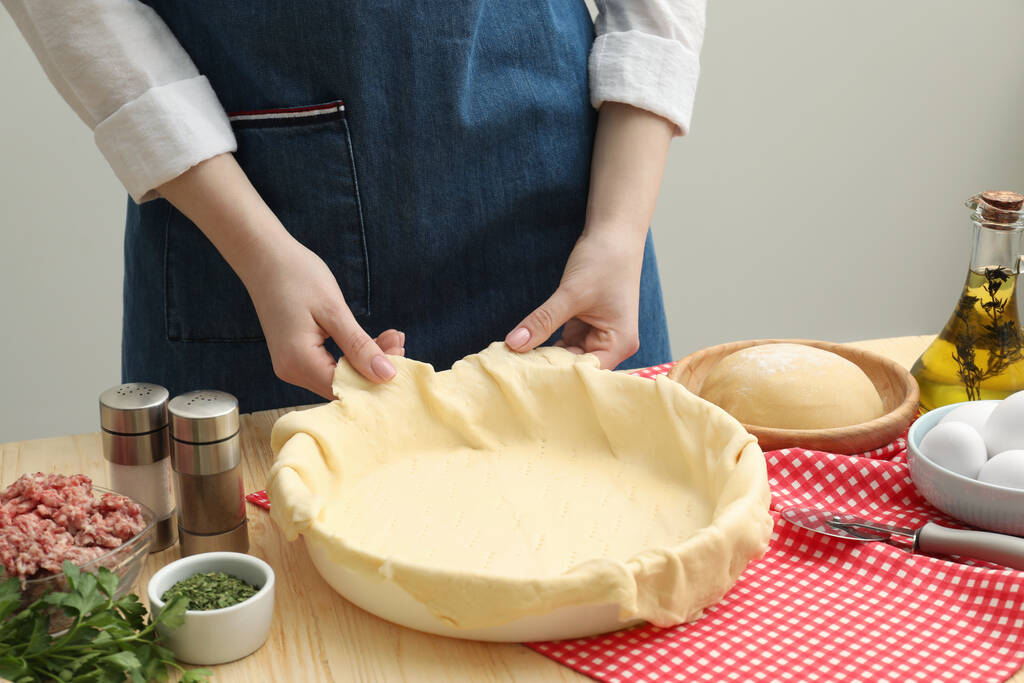 Woman putting dough for meat pie into baking dish at wooden table, closeup - Photo, Image