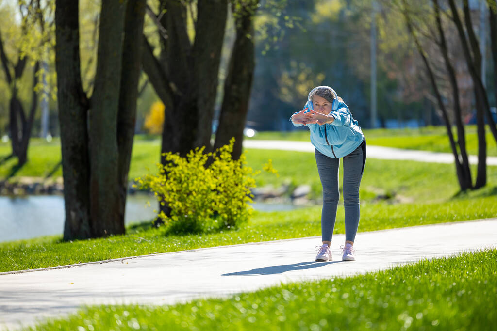 Antrenman yapıyorum. Mavi ceketli kadın parkta yaslanıyor. - Fotoğraf, Görsel