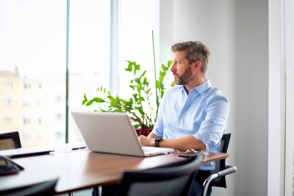 Homme d'affaires d'âge moyen inquiet assis dans un bureau moderne et utilisant un ordinateur portable pour le travail. Homme professionnel  - Photo, image