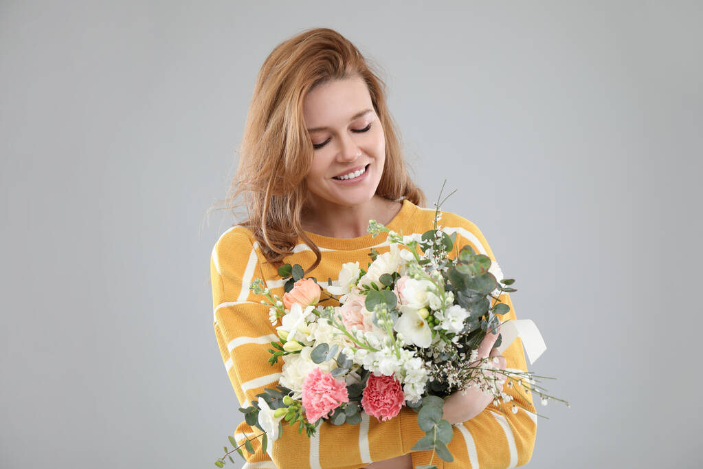 Beautiful woman with bouquet of flowers on grey background - Photo, Image