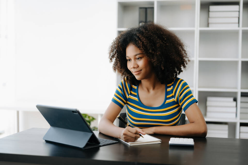  Bella donna africana che utilizza tablet e calcolatrice mentre si siede al suo posto di lavoro. Concentrato presso l'ufficio centrale - Foto, immagini
