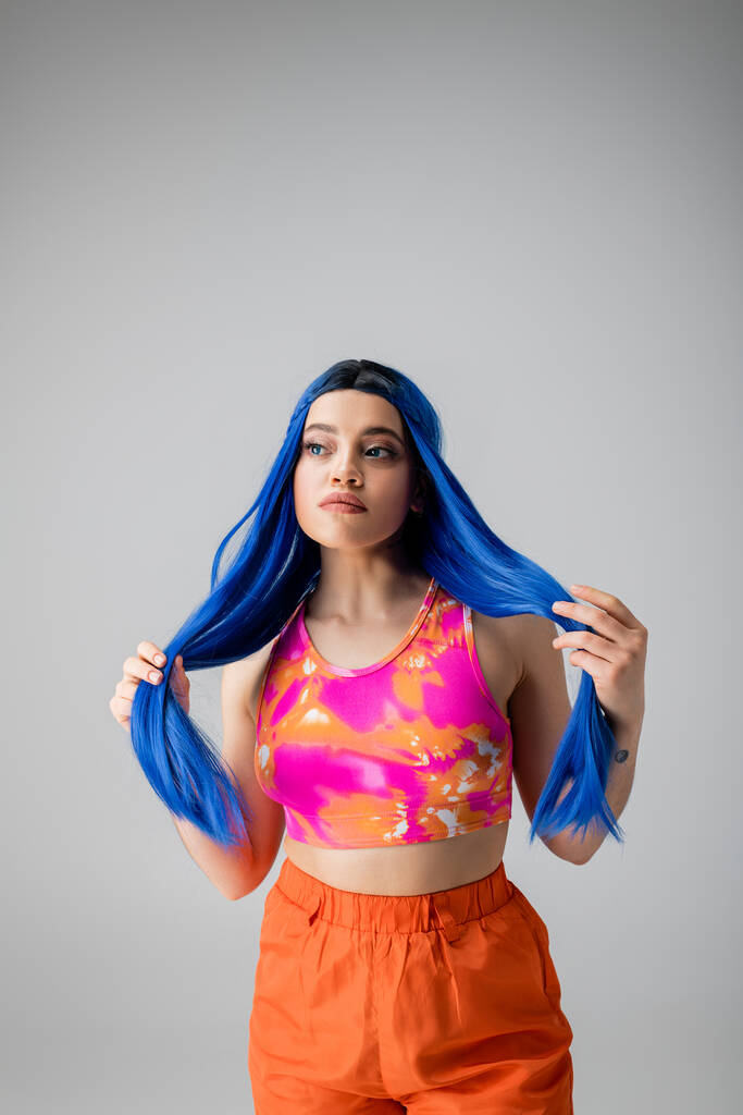 energia jovem, mulher jovem tatuada com cabelo azul posando em roupas coloridas em fundo cinza, individualismo, estilo moderno, moda urbana, cor vibrante, declaração de moda  - Foto, Imagem
