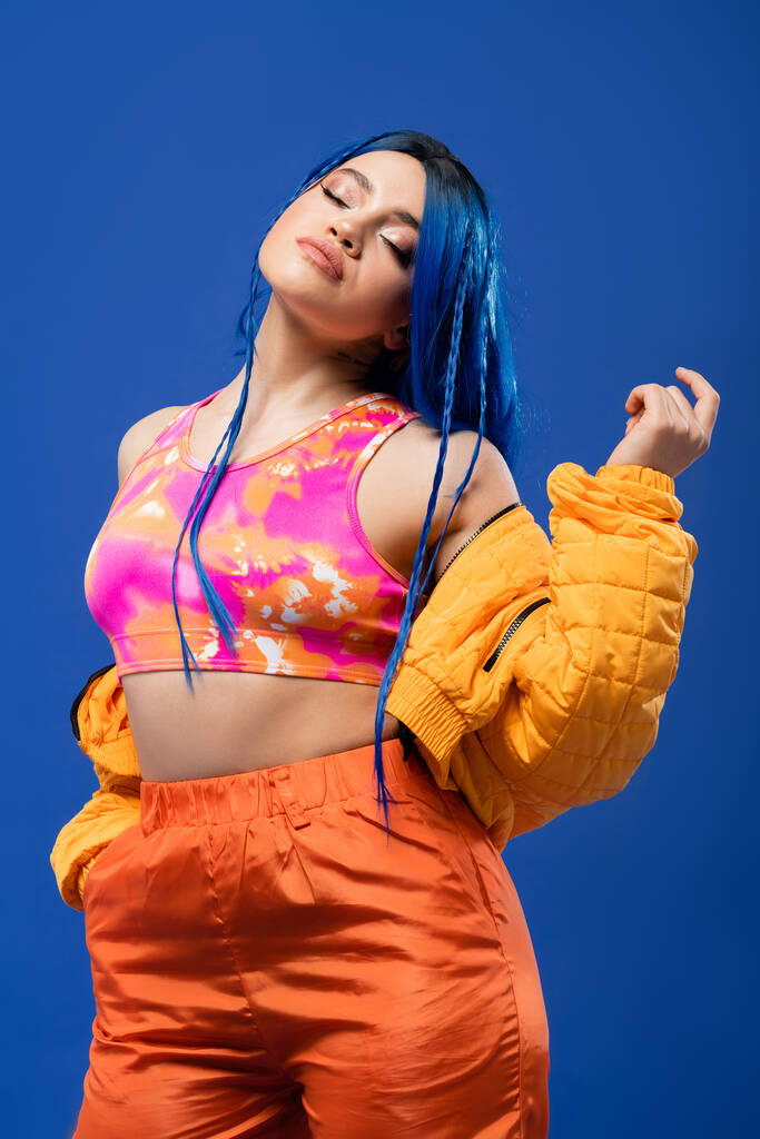 colorful clothes, dyed hair, female model with blue hair posing in puffer jacket on blue background, hand in pocket, vibrant color, urban fashion, individualism, young woman with funky look  - Photo, Image