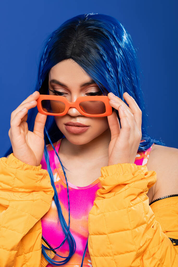 Mode-Statement, junges weibliches Model mit blauen Haaren und Zöpfen, trendige Sonnenbrille auf blauem Hintergrund, Generation Z, Rebellentyp, bunte Kleidung, Individualismus, moderne Frau  - Foto, Bild