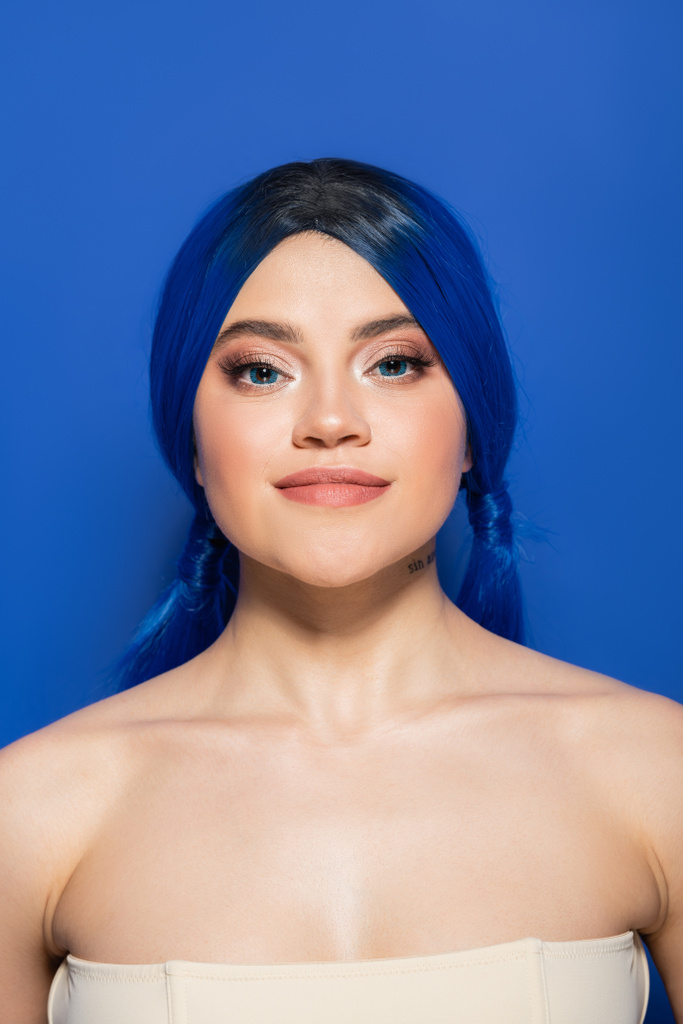 gloeiende huid concept, portret van zelfverzekerde jonge vrouw met levendig haar poseren met blote schouders op helderblauwe achtergrond, jeugd, individualisme, beauty trends, unieke identiteit, kijken naar camera - Foto, afbeelding