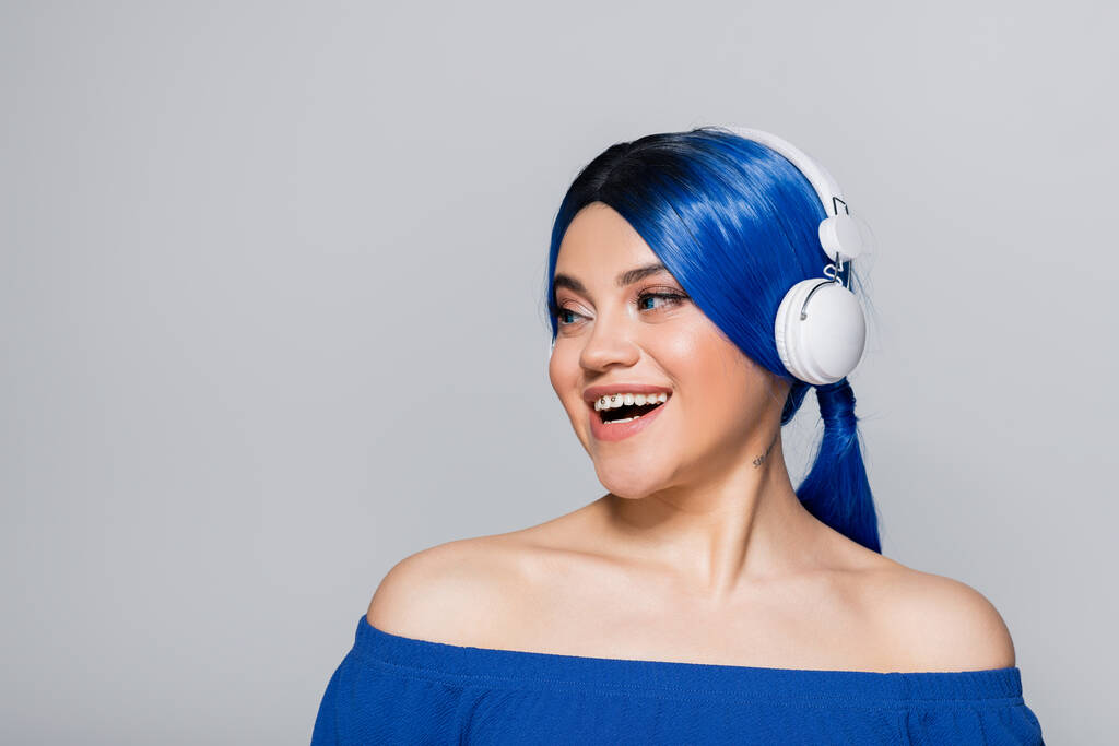 self expression, music lover, happy young woman with blue hair listening music in wireless headphones on grey background, vibrant youth, individualism, modern subculture, tattoo, sound  - Photo, Image