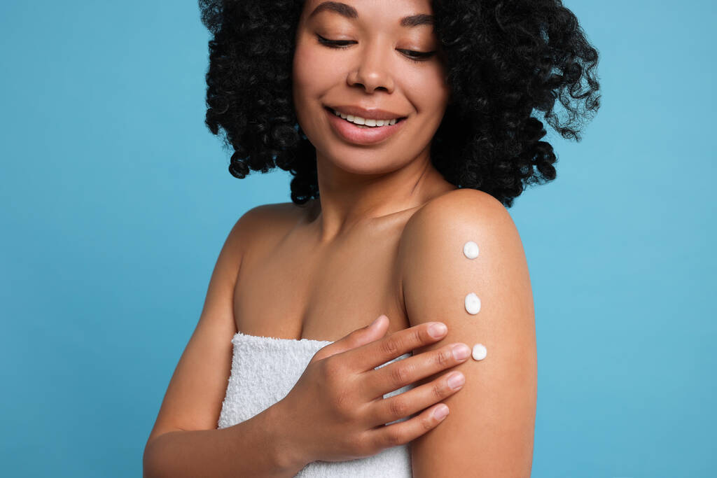 Young woman applying body cream onto shoulder on light blue background, closeup - Photo, image