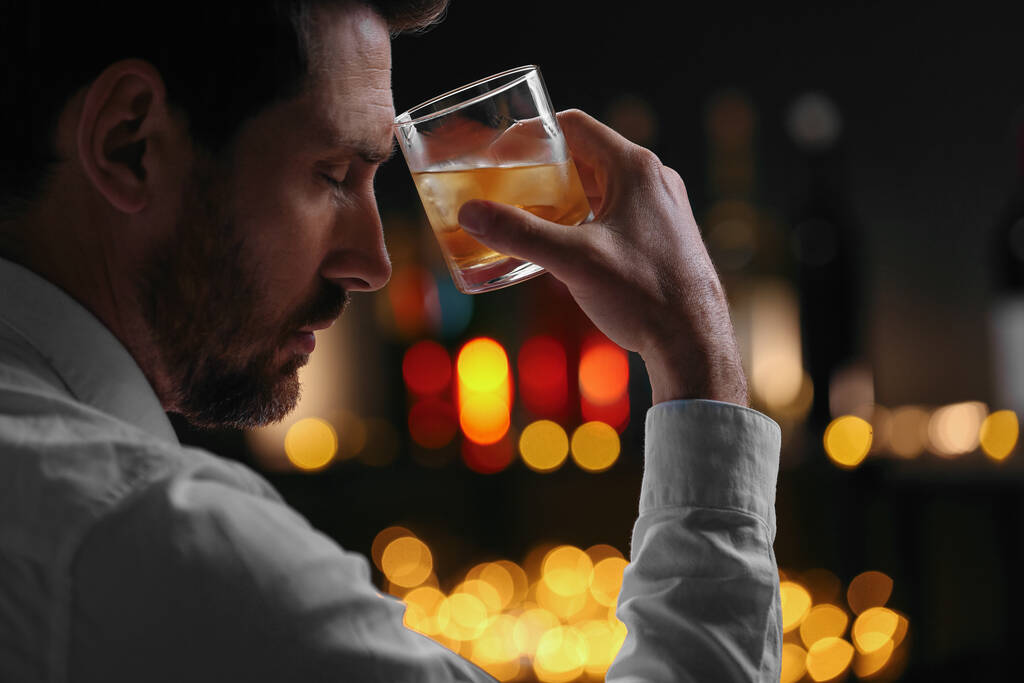 Hombre con vaso de whisky contra luces borrosas, primer plano - Foto, imagen