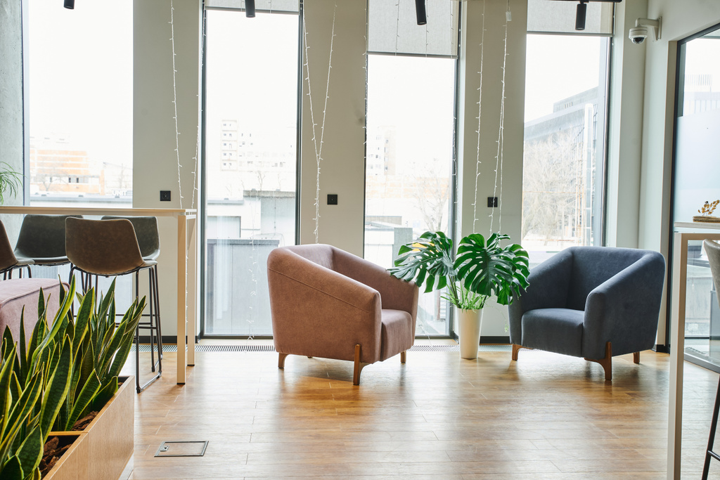 tágas irodai társalgó nagy ablakokkal, kényelmes és kényelmes fotelek, zöld és természetes növények modern coworking környezetben, munkaterület szervezés koncepció - Fotó, kép
