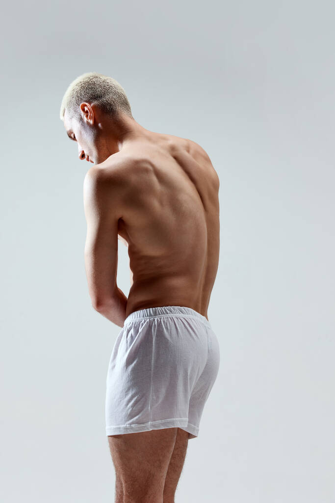 Strong, muscular, relief male back. Healthy body. Young handsome man posing in underwear against grey studio background. Concept of male natural beauty, body care, health, sport, fashion, ad - Photo, Image