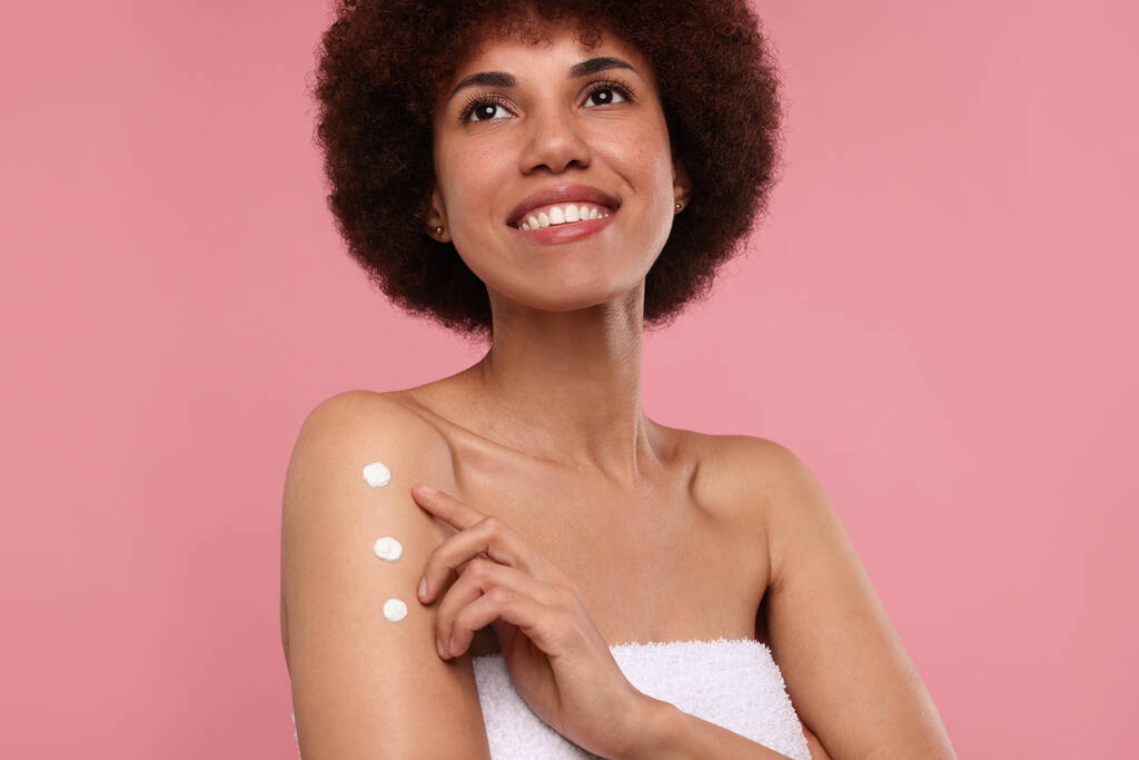 Krásná mladá žena použití tělo krém na paži na růžovém pozadí - Fotografie, Obrázek