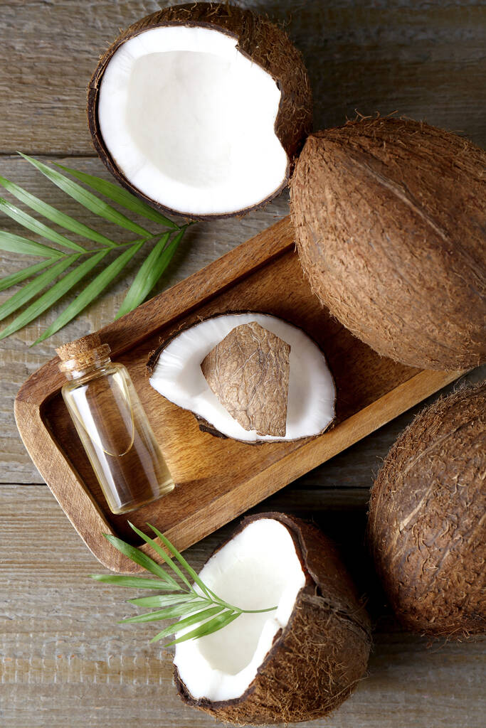 Бутылка органического кокосового масла для приготовления пищи, свежие фрукты и листья на деревянном столе, плоская укладка - Фото, изображение