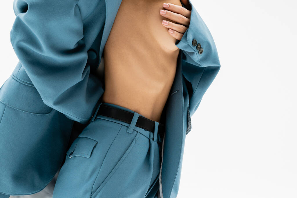 vrouwelijkheid en passie, gedeeltelijke weergave van verleidelijke vrouw in blauw pak op hemdloos lichaam en het bedekken van naakte borst met de hand terwijl poseren op grijze achtergrond, moderne zelfexpressie - Foto, afbeelding