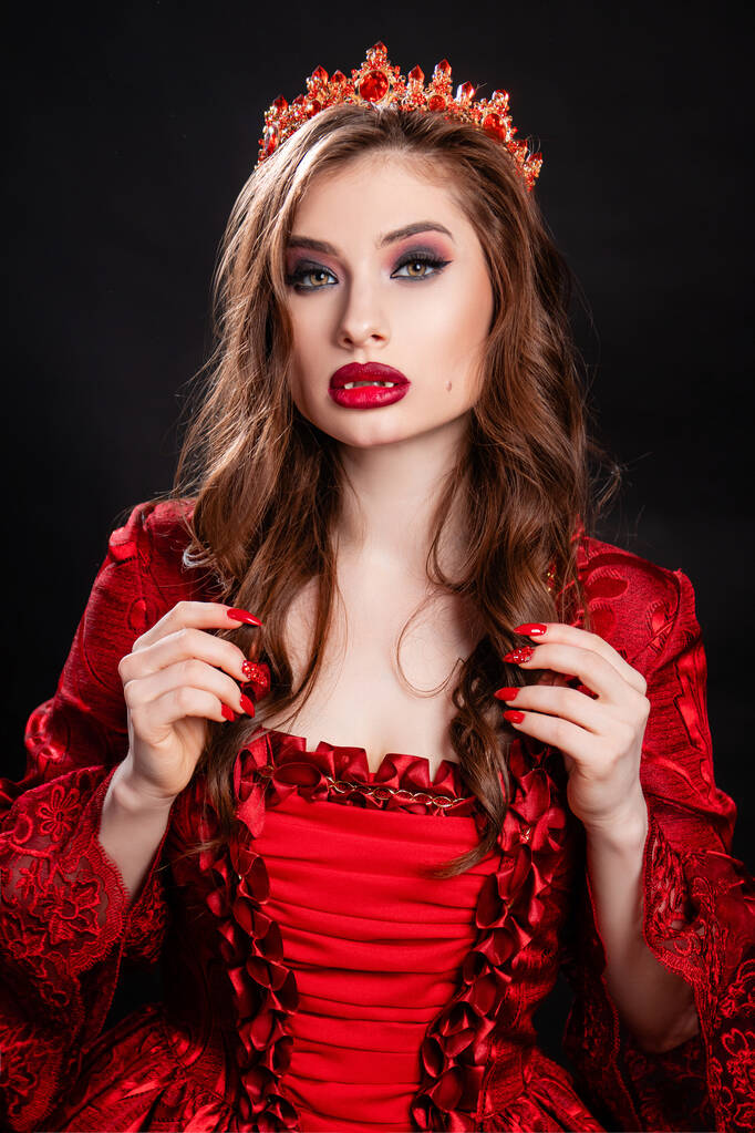Retrato de uma jovem e atraente mulher vampira em um vestido vermelho na era rococó com uma coroa na cabeça, posando isolada em um fundo escuro. - Foto, Imagem
