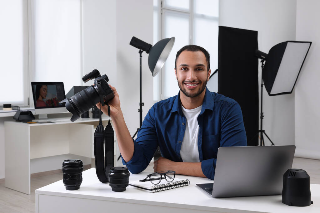 Mladý profesionální fotograf s fotoaparátem u stolu v moderním fotostudiu - Fotografie, Obrázek