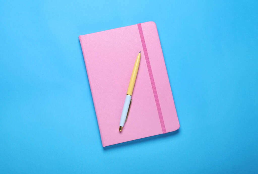 Zamknięty różowy notatnik i długopis na jasnoniebieskim tle, widok z góry - Zdjęcie, obraz