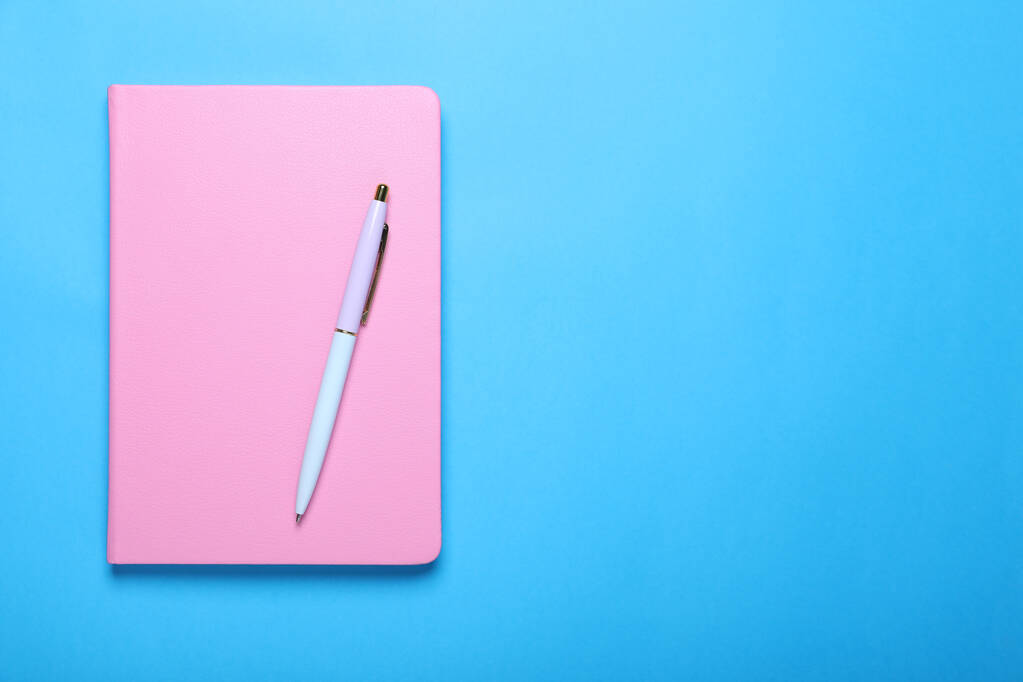 Geschlossenes rosafarbenes Notizbuch und Stift auf hellblauem Hintergrund, Draufsicht. Raum für Text - Foto, Bild