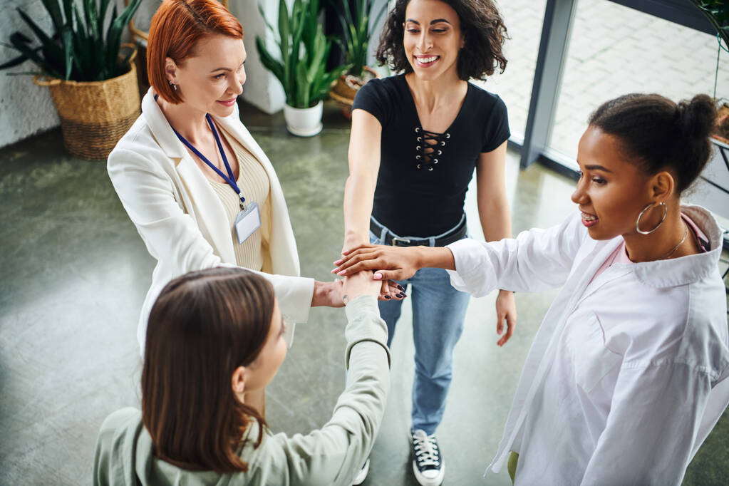 high angle view of multiethnic women and motivation coach joining hands while standing during psychology session, togetherness, moral support and mental wellness concept - Photo, Image