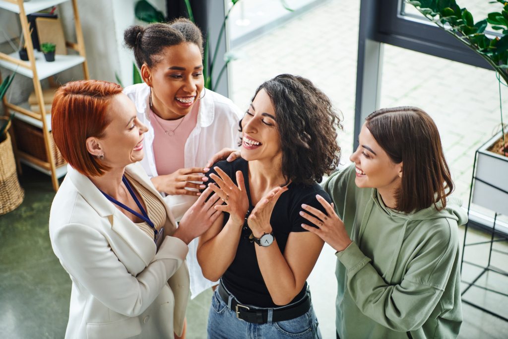 high angle view of happy motivation coach and multicultural girlfriends embracing happy multiracial woman smiling and gesturing with closed eyes, moral support and mental wellness concept - Photo, Image
