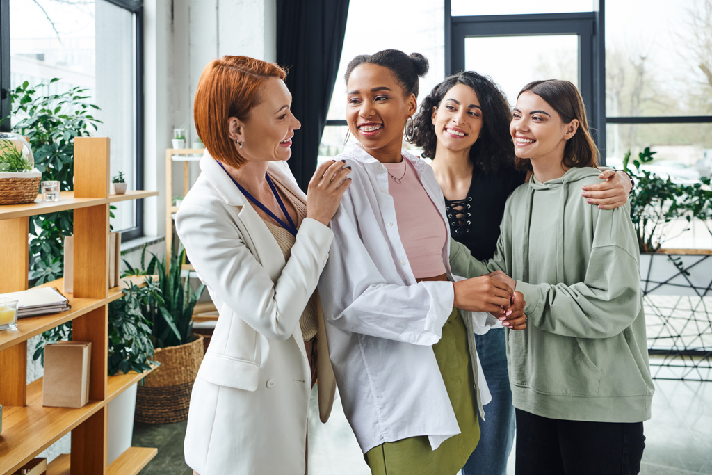 pleased psychologist looking at overjoyed african american woman near multiethnic girlfriends during motivation session in consulting room, female unity and support concept - Photo, Image