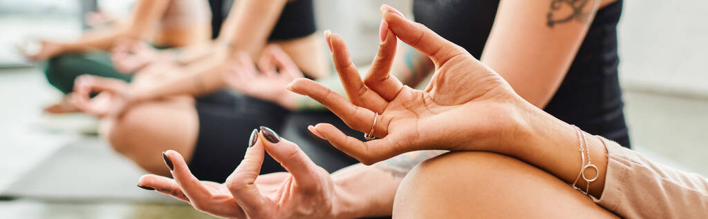 przycięty widok na zróżnicowaną grupę wielokulturowych przyjaciółek medytujących z gestem gyan mudra podczas zajęć jogi w siłowni, harmonii i koncepcji wellness, sztandar - Zdjęcie, obraz
