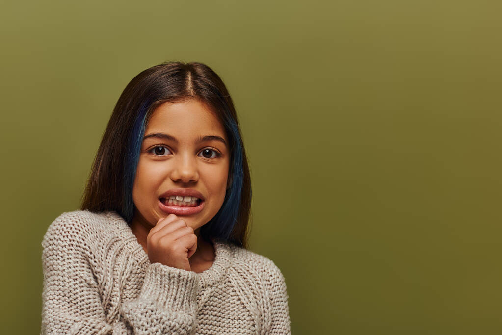 Portrait de fille préadolescente dégoûtée avec des cheveux colorés portant un pull tricoté confortable et regardant la caméra tout en se tenant debout et posant isolé sur vert, mode préadolescente moderne - Photo, image