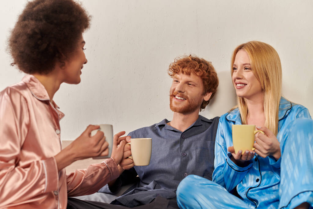 rapporto aperto concetto, poligamia, felice uomo chatta con donne interrazziale in pigiama, in possesso di tazze di caffè, amanti, bisessuale, comprensione, tre adulti, diversità culturale, accettazione  - Foto, immagini