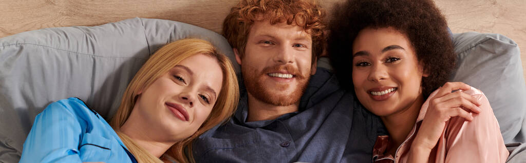 polygamy, alternative relationships, three adults, positive redhead man and multicultural women lying under blanket together, cultural diversity, acceptance, bisexual, open relationship, banner  - Photo, Image