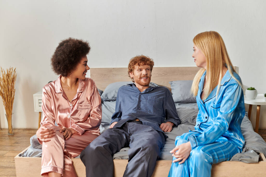 поліаморіальні коханці, розуміння, троє дорослих, рудий чоловік і багатокультурні жінки в піжамах сидять на ліжку вдома, культурне різноманіття, прийняття, бісексуальні, позитивні, відкриті відносини концепція  - Фото, зображення