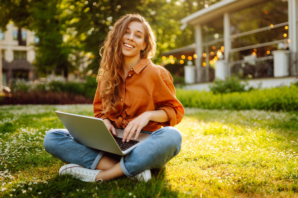 Krásná žena na volné noze sedí na zelené louce s laptopem. Online vzdělávání. Šťastná žena pobíhající venku a užívající si slunce. Koncept volného pohybu. - Fotografie, Obrázek
