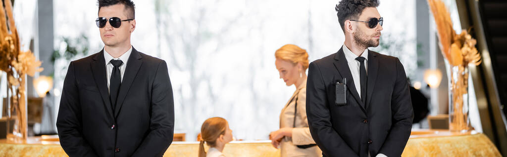 personal security, handsome bodyguards in suits and sunglasses protecting mother and child in hotel lobby, luxury lifestyle, woman and girl standing at reception desk, banner - Photo, Image