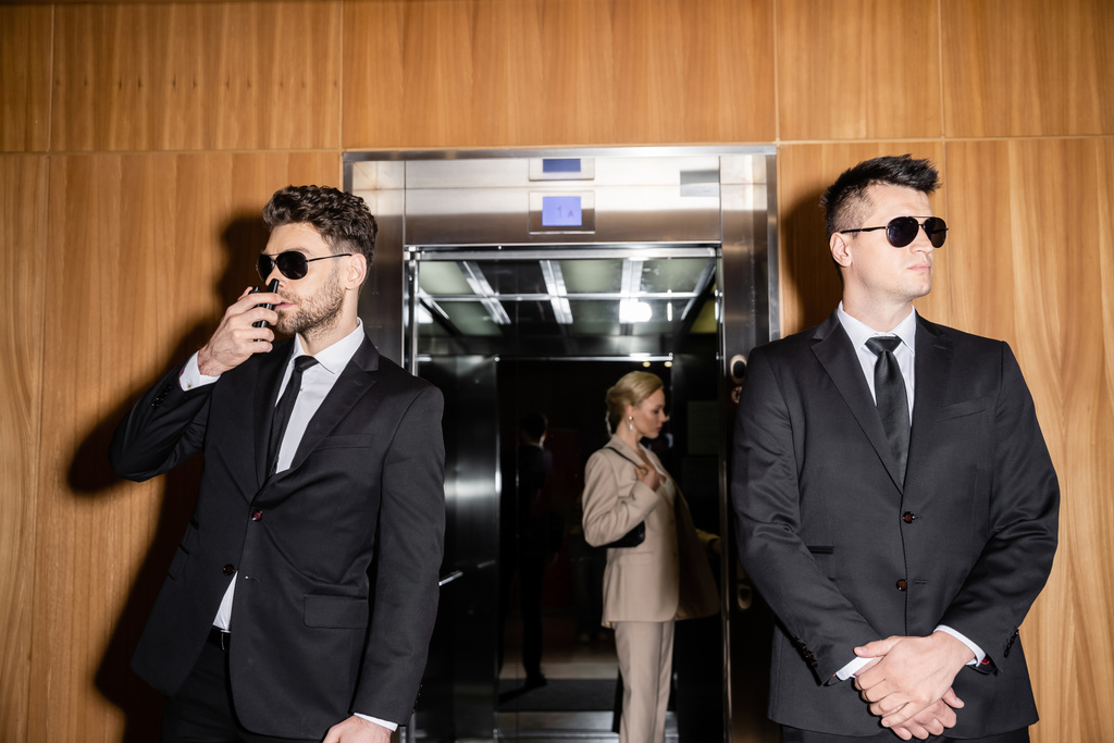 personal security and protection concept, blonde and successful woman with handbag standing inside of elevator next to bodyguards in suits and sunglasses, luxury hotel, private safety  - Photo, Image