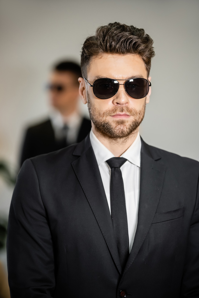 Bodyguard-Service, gutaussehender Mann mit Sonnenbrille und schwarzem Anzug mit Krawatte, Hotelsicherheit, Sicherheitsmanagement, Überwachung und Wachsamkeit, uniformierter Wachmann im Dienst, professionelle Kopfschüsse - Foto, Bild