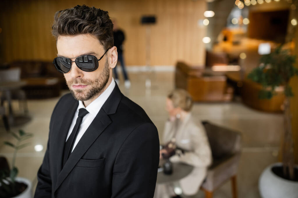 private security service, personal safety concept, handsome bodyguard in formal wear and sunglasses protecting safety of female client on blurred background, mother and daughter in cafe  - Photo, Image