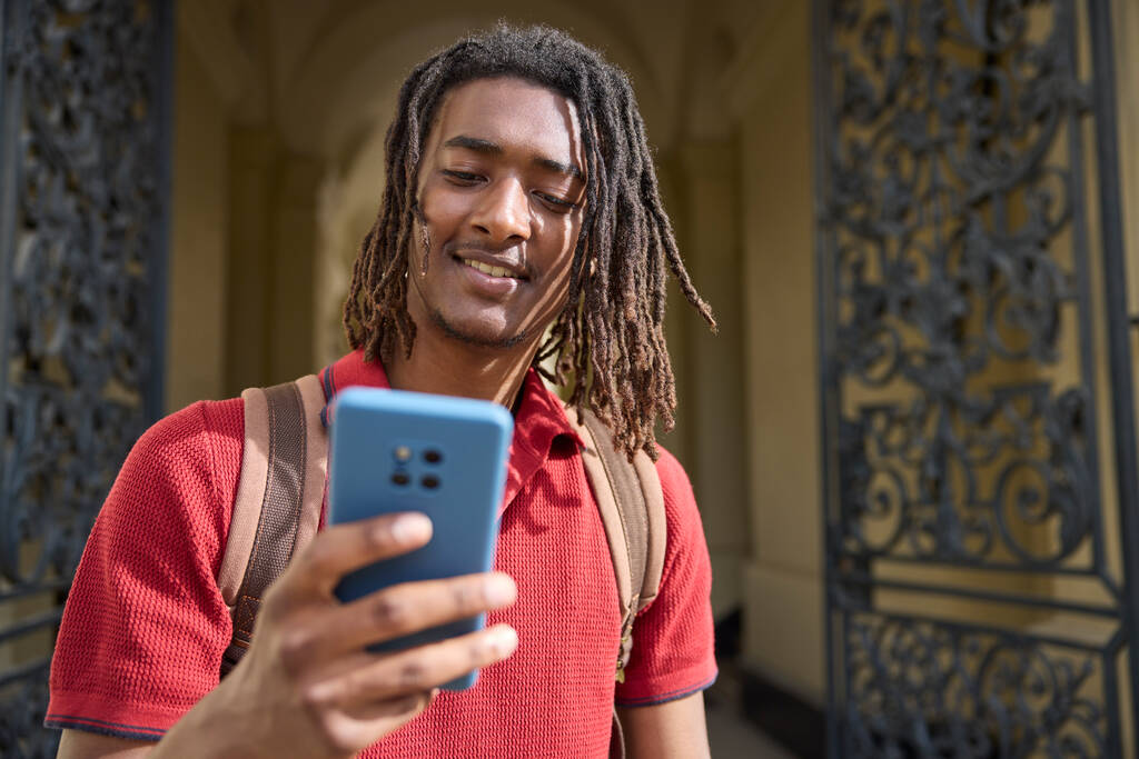 男性学生がオックスフォード大学外の携帯電話でメッセージやソーシャルメディアをチェック｜UK - 写真・画像