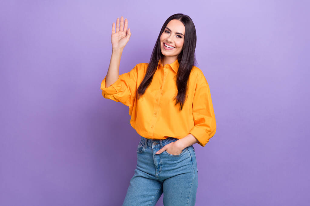 Фото позитивної веселої дружньої ділової жінки в помаранчевій сорочці джинсові хвилі долоні привітання ізольовані на фіолетовому кольоровому фоні. - Фото, зображення