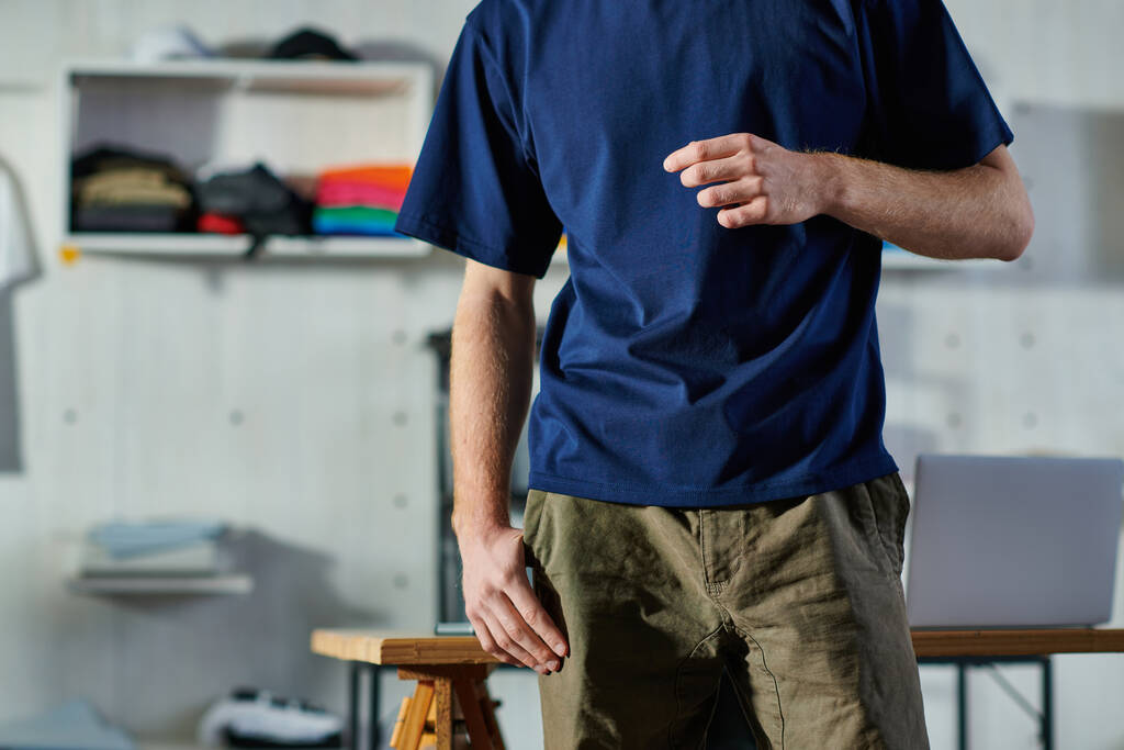Ausgeschnittene Ansicht eines jungen Handwerkers in lässiger Kleidung, der in der Nähe des Arbeitstisches im verschwommenen Druckeratelier im Hintergrund steht, praktisches Unternehmertum-Konzept  - Foto, Bild