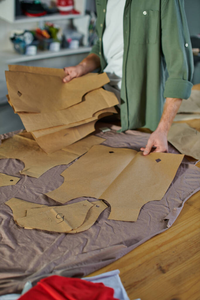 Vista recortada de artesanos sosteniendo patrones de costura cerca de la tela en la mesa mientras trabajan en un estudio de impresión borrosa, dueño de un negocio multitarea administrando múltiples proyectos - Foto, imagen