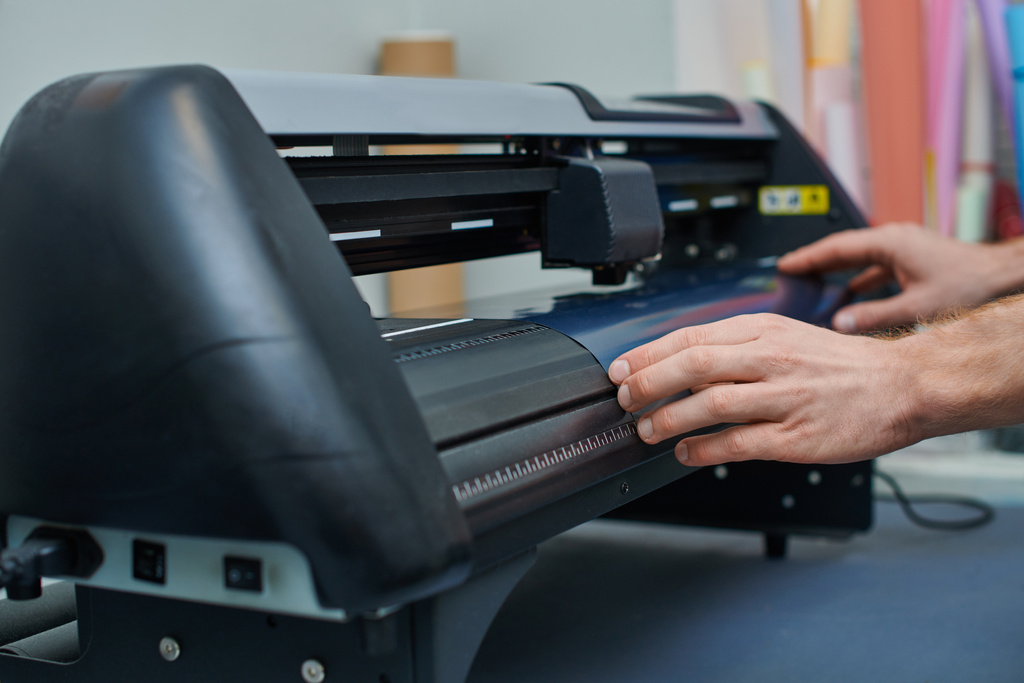 Ausgeschnittene Ansicht junger Handwerker, der Schicht in der Nähe Siebdruckmaschine hält, während er im Druckstudio arbeitet, Kleinunternehmer, der an einem Projekt arbeitet, Kreativität  - Foto, Bild