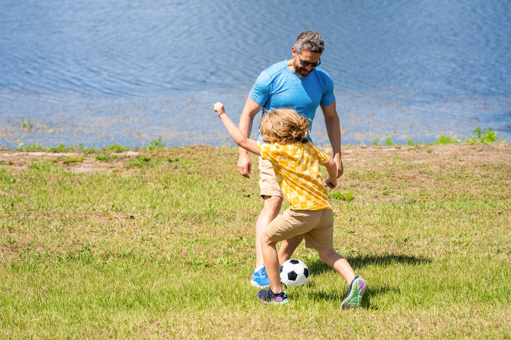Boldog gyerekkort, amikor a fiú apával játszik. Apa és fia nyári program. A fiúnak szabadtéri kapcsolata van apával. Apa és fia élvezze a barátságos focimeccset. emlékeket gyűjteni a természetben. - Fotó, kép