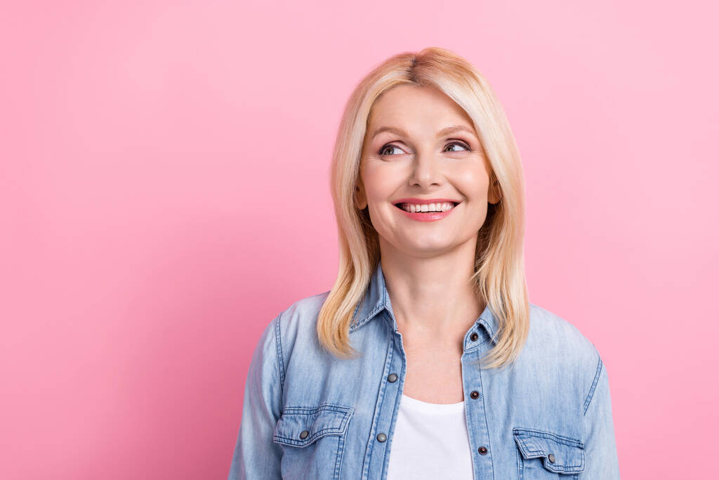 Foto van mooie senior blonde dame stralend glimlachend uitziende kant lege ruimte nieuwsgierig dragen denim shirt geïsoleerde roze kleur achtergrond. - Foto, afbeelding