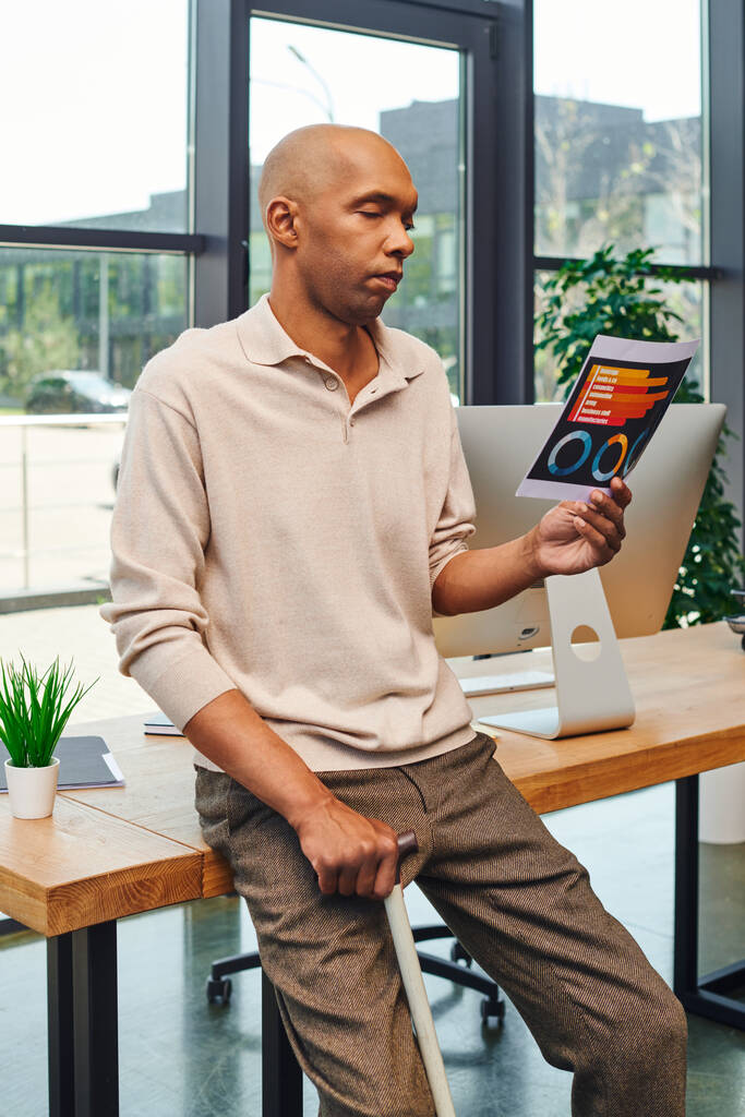 ένταξη, σύνδρομο μυασθένεια gravis, τολμηρός Αφροαμερικάνος επιχειρηματίας που στέκεται με μπαστούνι και κοιτάζει διαγράμματα κοντά στην οθόνη του υπολογιστή, σκουρόχρωμος υπάλληλος γραφείου με περιστασιακή ενδυμασία - Φωτογραφία, εικόνα