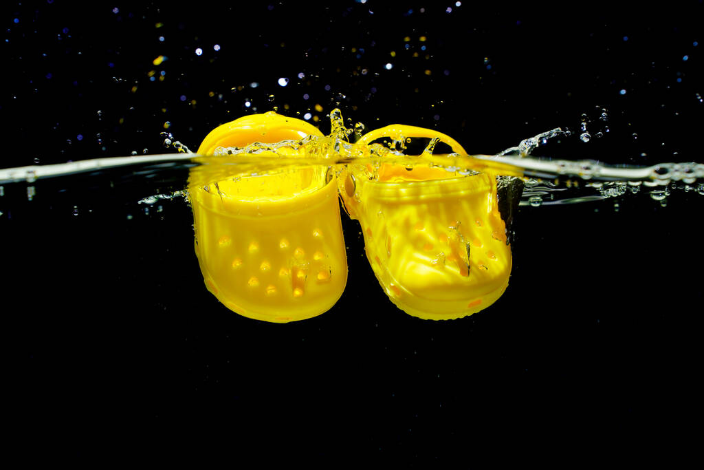 Kijev, Ukrajna - június 6, 2023: Apró sárga Crocs cipők víz alá merült fröccsenő - Fotó, kép
