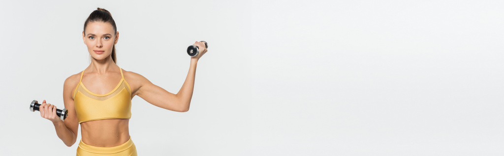 Sportlerin in Fitnessbekleidung blickt in die Kamera, Training mit Hanteln isoliert auf weiß, Banner - Foto, Bild