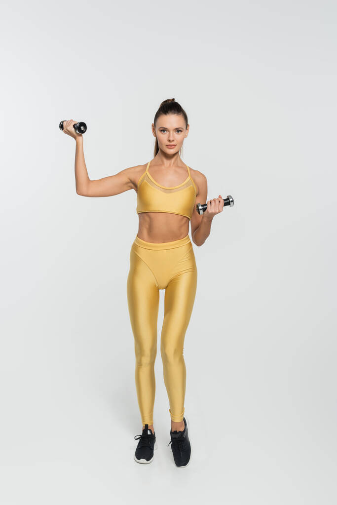 žena ve sportovním oblečení trénink s činky na bílém pozadí, síla a odhodlání koncept - Fotografie, Obrázek