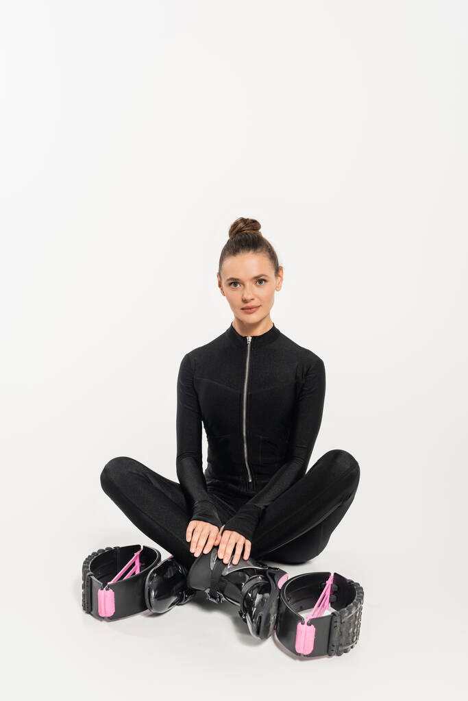 laarzen voor het springen, sportvrouw in zwart jumpsuit zitten met gekruiste benen, kangoo springen,  - Foto, afbeelding