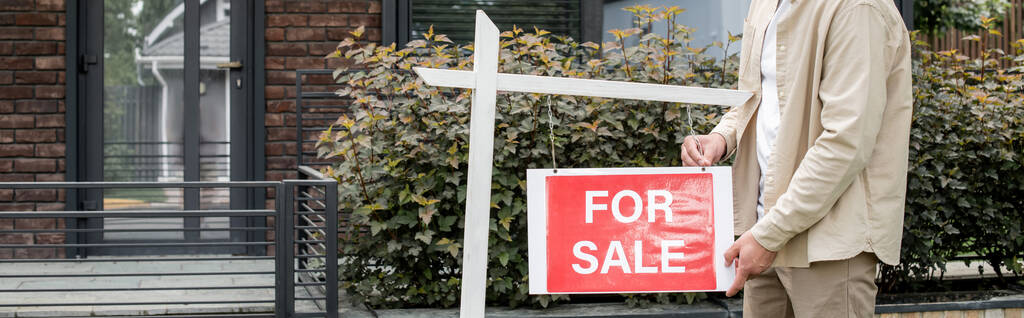 vista recortada de la propiedad inmobiliaria colgando en venta letrero cerca de la casa de la ciudad contemporánea, pancarta - Foto, imagen