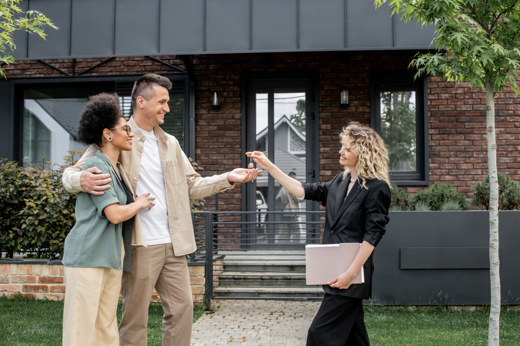 Immobilienmakler mit Ordner übergibt Schlüssel an überglückliches Paar in der Nähe des neuen Stadthauses - Foto, Bild